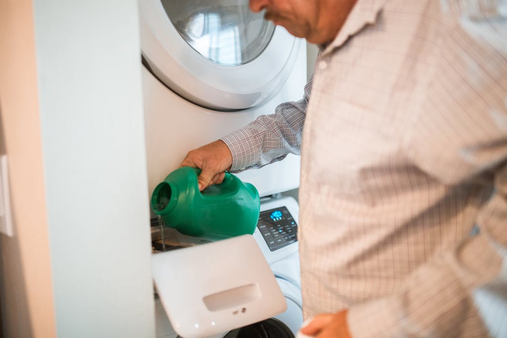 Idoso despejando detergente no compartimento de uma máquina de lavar frontal de alta eficiência, capturando o cuidado na preparação de um ciclo de lavagem, parte da rotina do uso de eletrodomésticos domésticos.